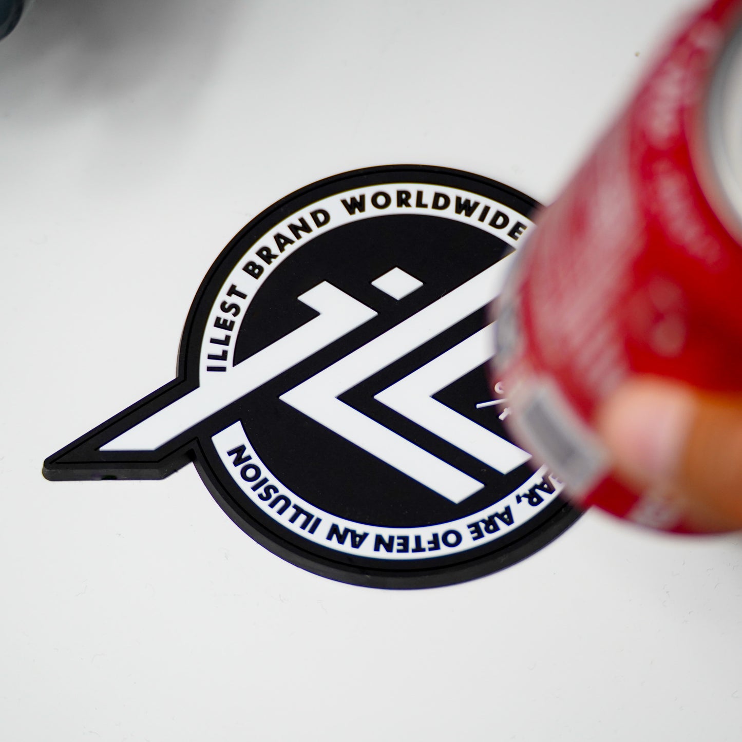 Black and white Illest brand coaster with the quote "limits like fear are often an illusion" visible, partially obscured by a red can.