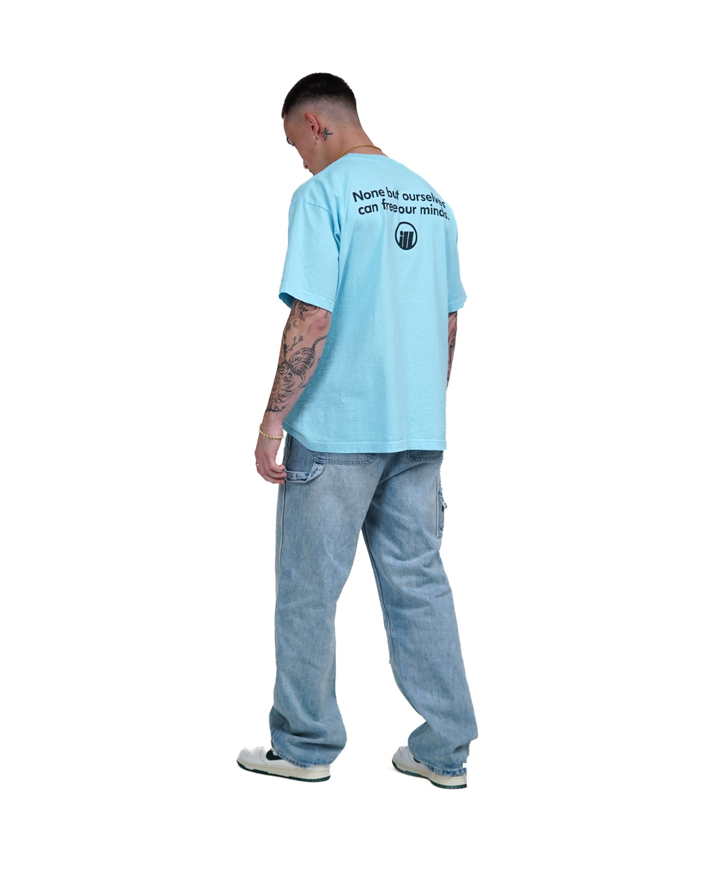 Man wearing a light blue Illest Bold Logo Miami Blue T-shirt with text on the back, paired with baggy jeans and sneakers.