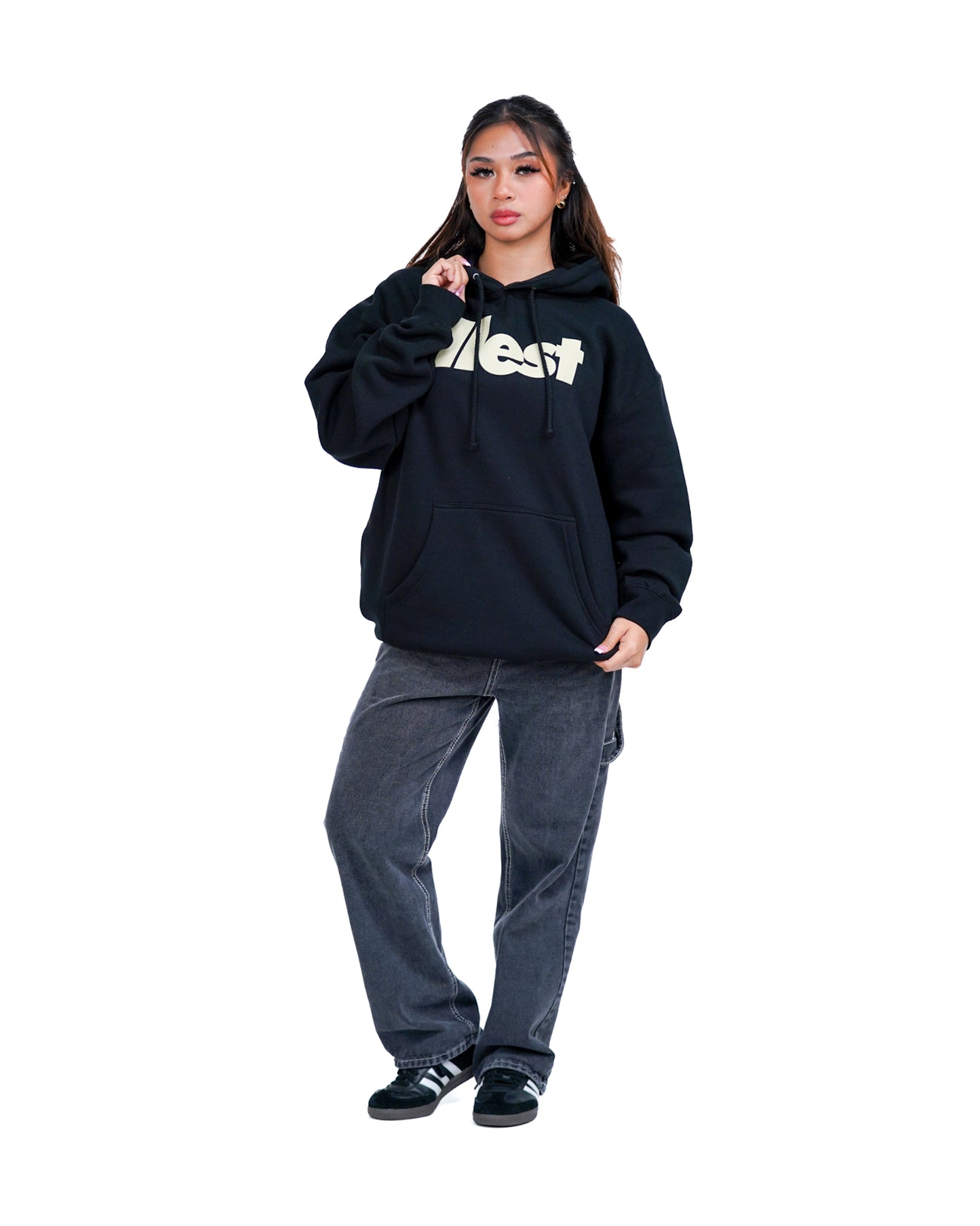 Woman wearing a black Illest Bold Logo hoodie with a large front pocket, paired with gray baggy jeans and black sneakers.