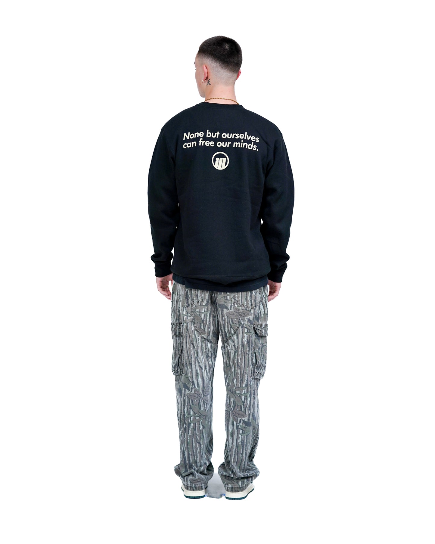 Back view of a person wearing a black crewneck sweatshirt with the Illest logo and text on the back, paired with patterned cargo pants.
