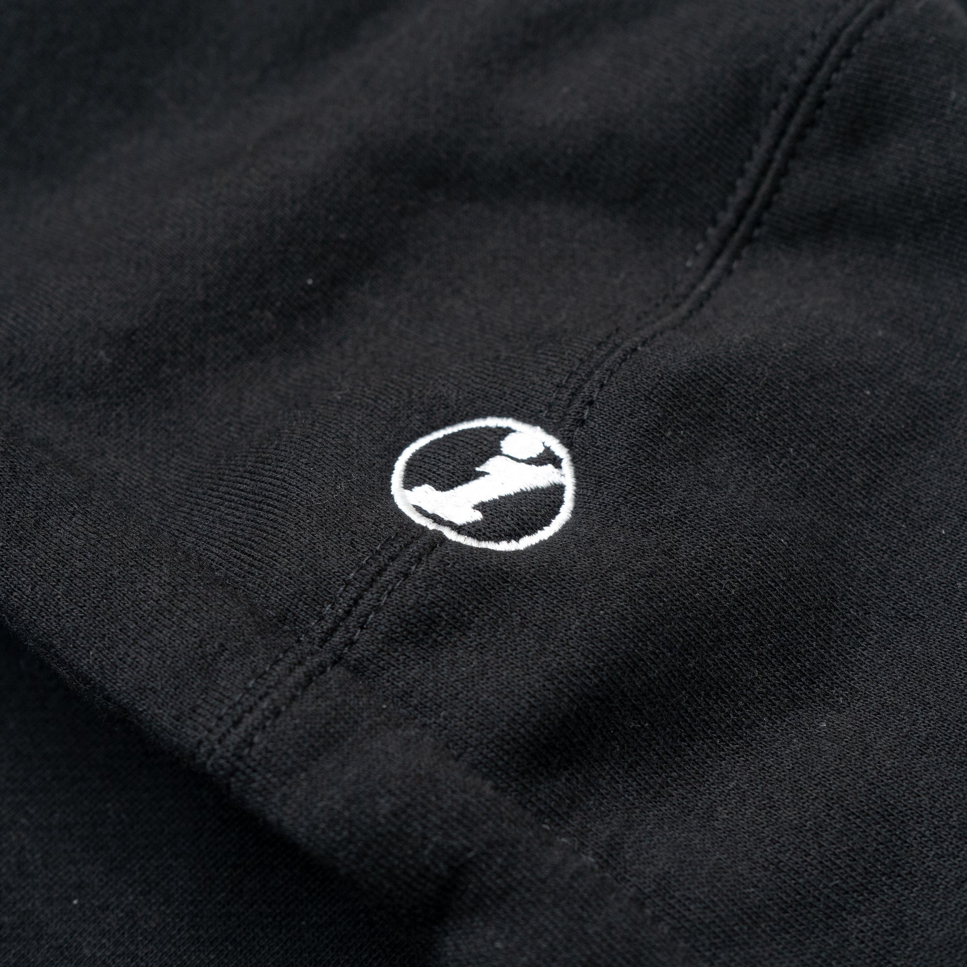 Close-up of a black Illest Essentials Hoodie featuring a small white embroidered logo of a stylized figure inside a circle.