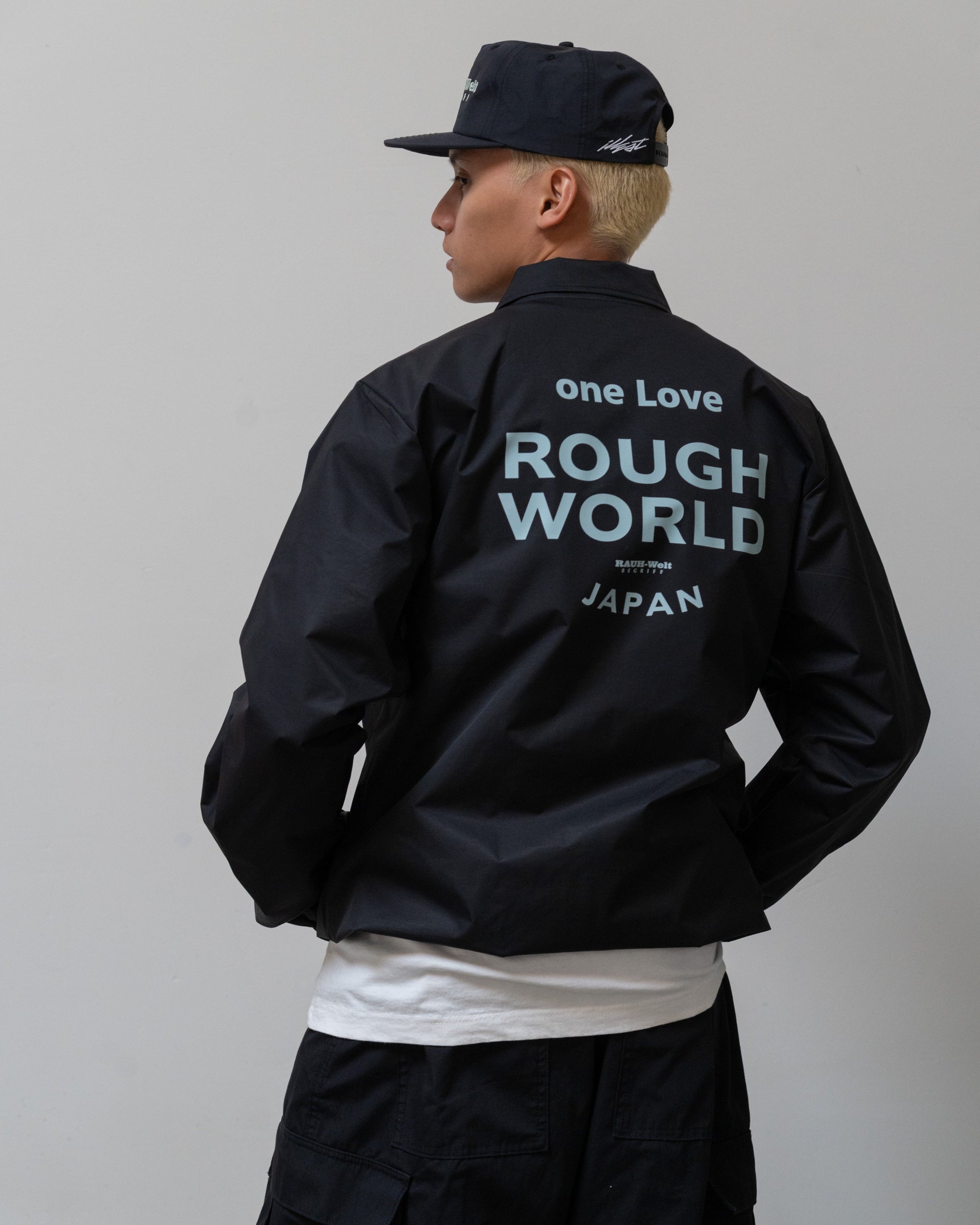 Back view of a person wearing a black Illest Rough-World Coach Jacket with large light blue text reading "one Love Rough World Japan" on the back.