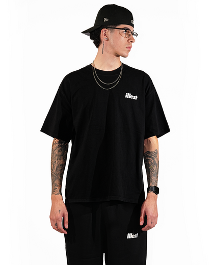 Male model wearing a faded black T-shirt and matching shorts with "illest" branding, accessorized with chains, glasses, and a black cap.