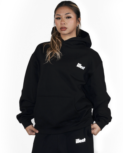 Woman wearing a black Illest Prime Essentials hoodie and matching sweatpants, both featuring the Illest logo in white.