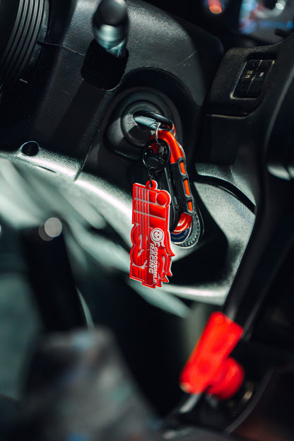 Red rubber keychain featuring ILLEST x GOODSMILE racing logo, attached to car keys in a vehicle ignition.