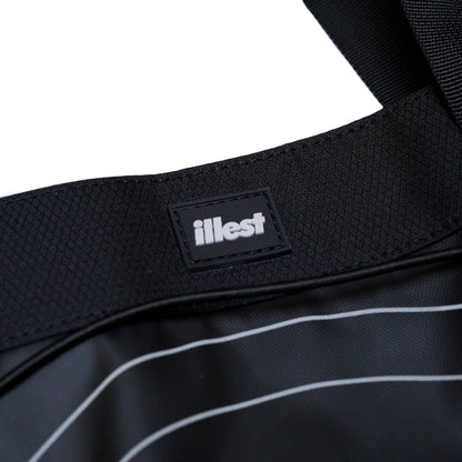 Close-up of the black Illest Travel Tote Bag showing the textured fabric, white piping detail, and the Illest brand label.