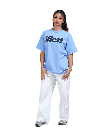 Woman wearing a periwinkle Illest bold logo T-shirt with white cargo pants and sneakers, standing against a white background.