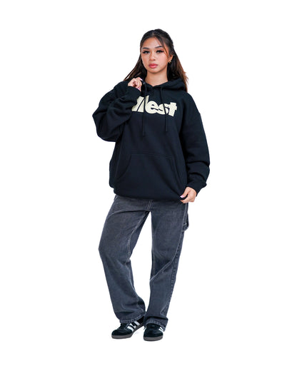 Woman wearing a black Illest Bold Logo hoodie with a large front pocket, paired with gray baggy jeans and black sneakers.