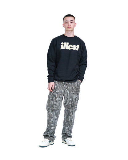 Young man wearing a black crewneck sweatshirt with "Illest" logo, patterned cargo pants, and white sneakers.