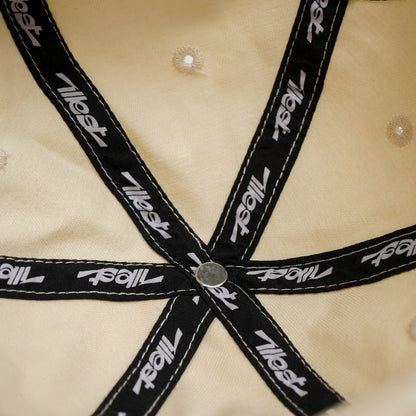 Close-up of a beige dad cap with black straps featuring the Illest logo, fastened with a metal rivet at the center.