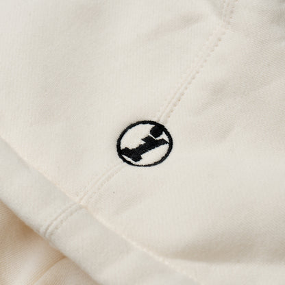 Close-up of a cream-colored Illest Essentials Hoodie featuring a small black and white embroidered logo on the fabric.