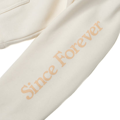 Close-up of an off-white hoodie sleeve with "Since Forever" printed in light peach text, showcasing a stylish casual design.