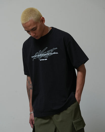 Young man wearing a black Illest Rough-World T-shirt with graphic text, standing against a plain background.