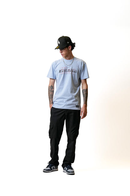 Male model wearing a light gray Illest Racing Factory T-shirt, black cargo pants, sneakers, a black cap, and layered necklaces.