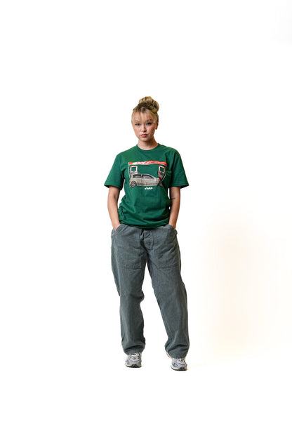 Young woman wearing a green Illest Filling Station T-shirt with a graphic design, paired with loose gray pants and sneakers.