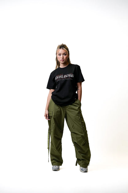 Woman wearing a black Illest Racing Factory T-shirt and green cargo pants, standing against a plain white background.