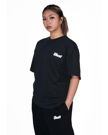 Model wearing a faded black Illest Prime Essentials T-shirt and matching pants, featuring white Illest branding on chest and thigh.