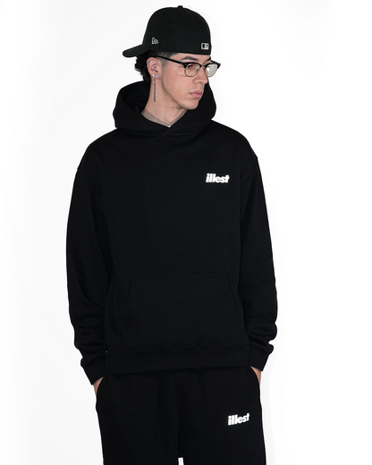 Male model wearing a black Illest Prime Essentials hoodie and matching sweatpants, accessorized with glasses, earrings, and a black cap.