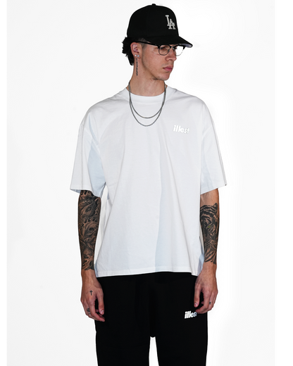 Male model wearing a white faded T-shirt with "illest" logo, black cap with "LA" logo, glasses, layered necklaces, and tattoos on arms.