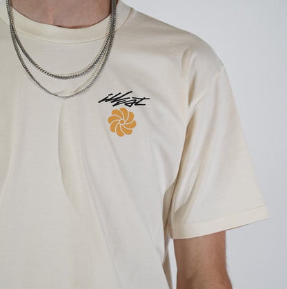 Close-up of a cream-colored T-shirt featuring the Illest logo and a stylized orange flower graphic on the chest, worn with layered silver chains.