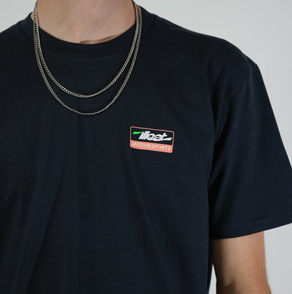 Close-up of a person wearing a black Illest No Limits T-shirt with a small Illest Motorsports logo on the chest, layered with silver chains.