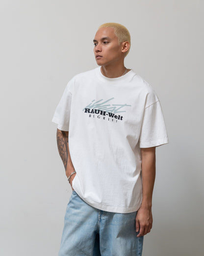 White T-shirt with black and gray graphic text reading Illest Rough-World White Tee, worn by a person with short blond hair and tattoos.